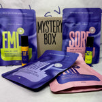 4 bath salts and 2 oil roller bottles in front of a box with Mystery Box written on it.